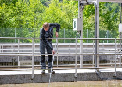 Mitarbeiter entnimmt mit einer Schöpfstange eine Probe aus dem Belebungsbecken