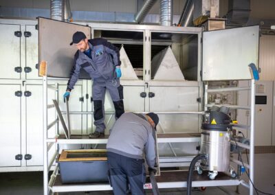 Zwei Mitarbeiter reinigen den Klärschlammtrockner mit einem Industriesauger