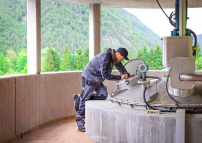 Mitarbeiter kontrolliert eine Armatur auf dem Faulturm, im Hintergrund die Berge