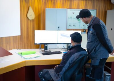 Zwei Mitarbeiter vor dem Anlagenschema und den Monitoren der Leitwarte