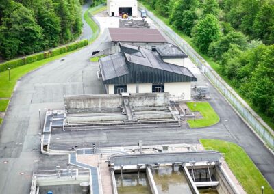 Luftaufnahme der Kläranlage mit Becken und Betriebsgebäude, im Hintergrund das Tal und die Berge