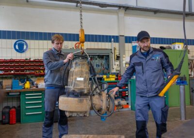Zwei Mitarbeiter mit einer am Kran hängenden Pumpe
