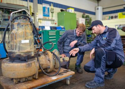 Zwei Mitarbeiter begutachten eine Pumpe am Boden